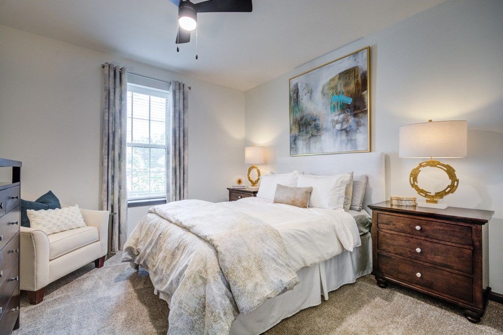 A bedroom with a large bed, a white chair, and a painting on the wall.