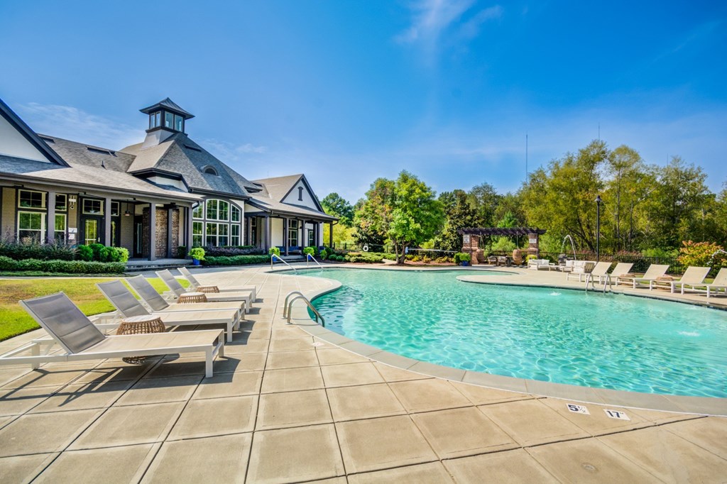 A large swimming pool is surrounded by lounge chairs in front of a house.