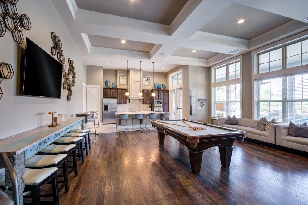 A billiard table is in the middle of a room with a bar and a television.