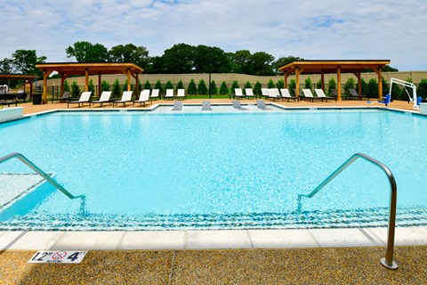 A swimming pool with a metal ladder and a poolside with chairs.