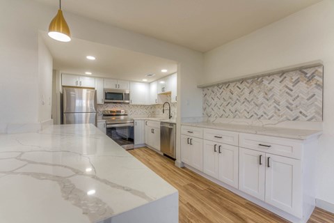 A kitchen with white cabinets and a marble countertop.