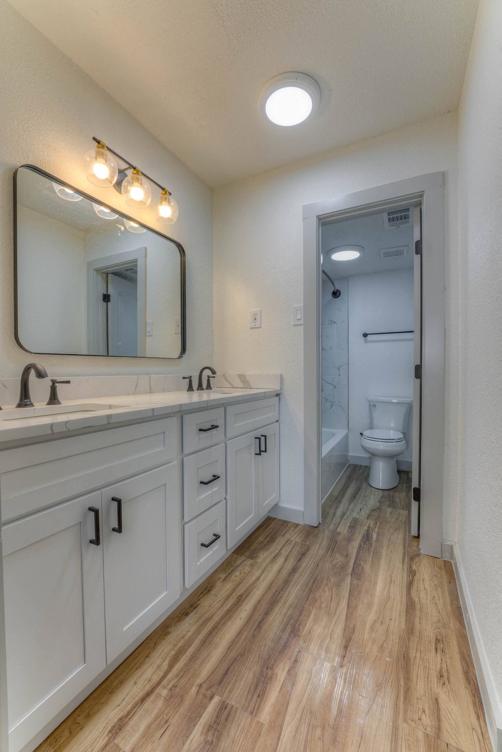 A bathroom with a wooden floor and white walls.at The Garden District Apartments, Tennessee  