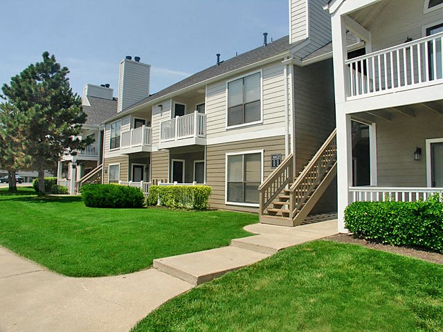 Meticulously maintained grounds with mature trees surround the soft tan paint and brick exterior apartment homes at Hampton Woods, Shawnee