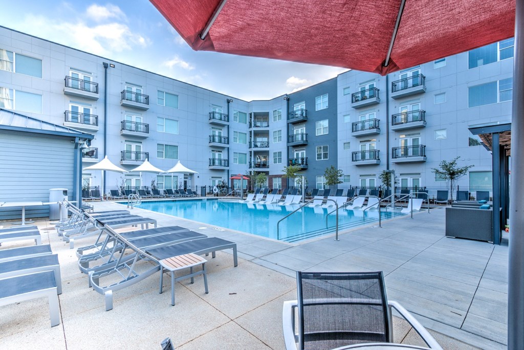 A pool area with sun loungers and a red umbrella.