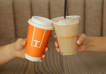two hands holding two coffee drinks in front of a wooden table at Livano Avondale, Arizona