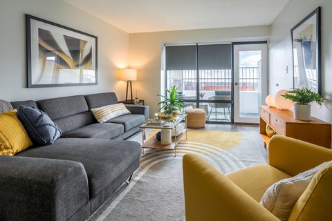 A grey couch with yellow pillows sits in a living room with a large window.