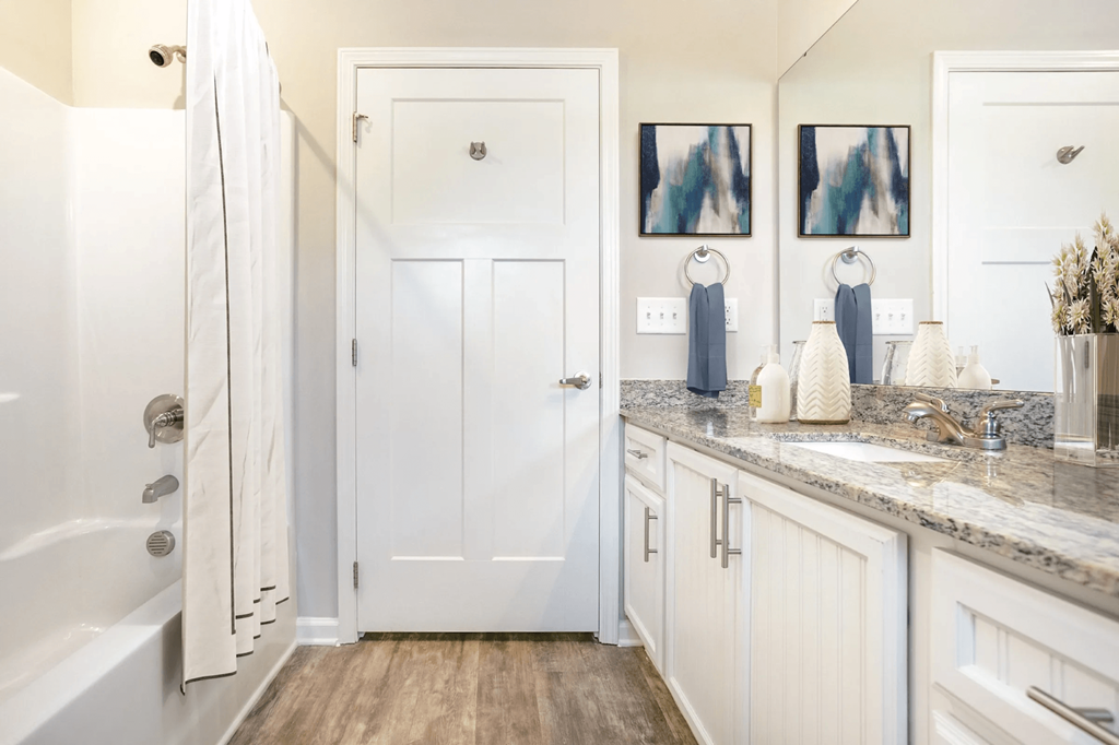 A white bathroom with a tub, sink, and mirror at Henley at Mirror Lake Apartments, Georgia