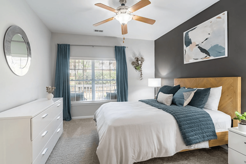 A bedroom with a large bed, a ceiling fan, and a window with curtains.