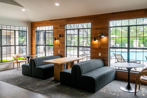 A black couch and chair are in a room with a wooden floor and a pool outside the window.