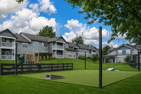 A playground area with a slide and a green surface is surrounded by a fence and houses.