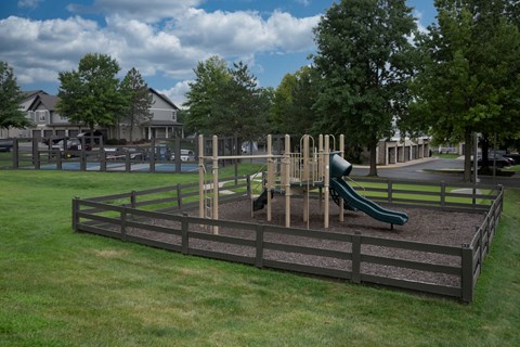A playground with a green slide and a brown fence.