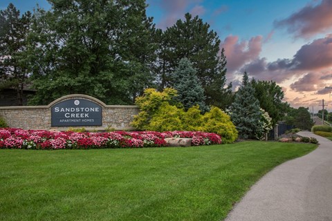 A sign for Sandstone Creek Apartment Homes is surrounded by flowers and greenery.