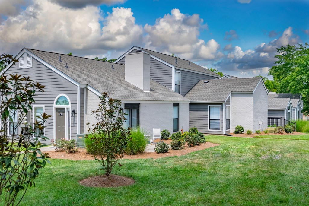 A house with a grey roof and a small tree in front.