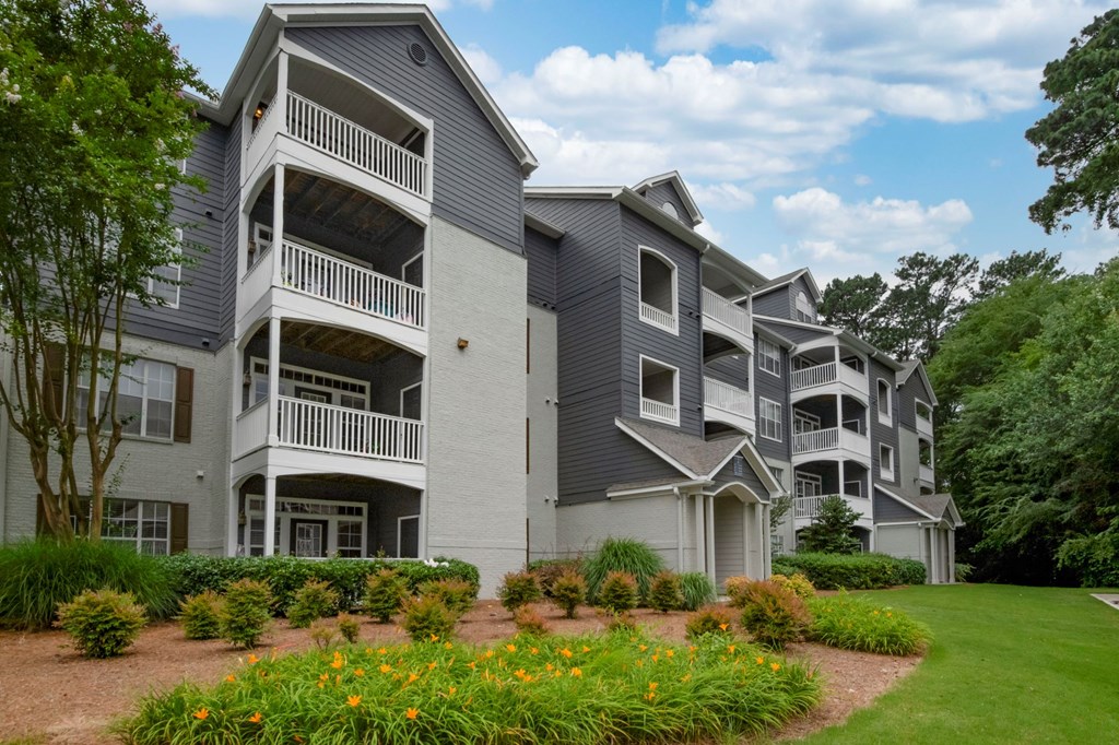 A grey apartment building with balconies and flower beds in front.