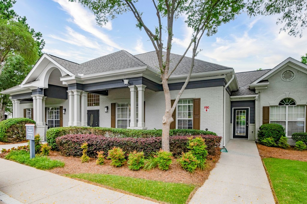 A white house with a grey roof and a tree in front.