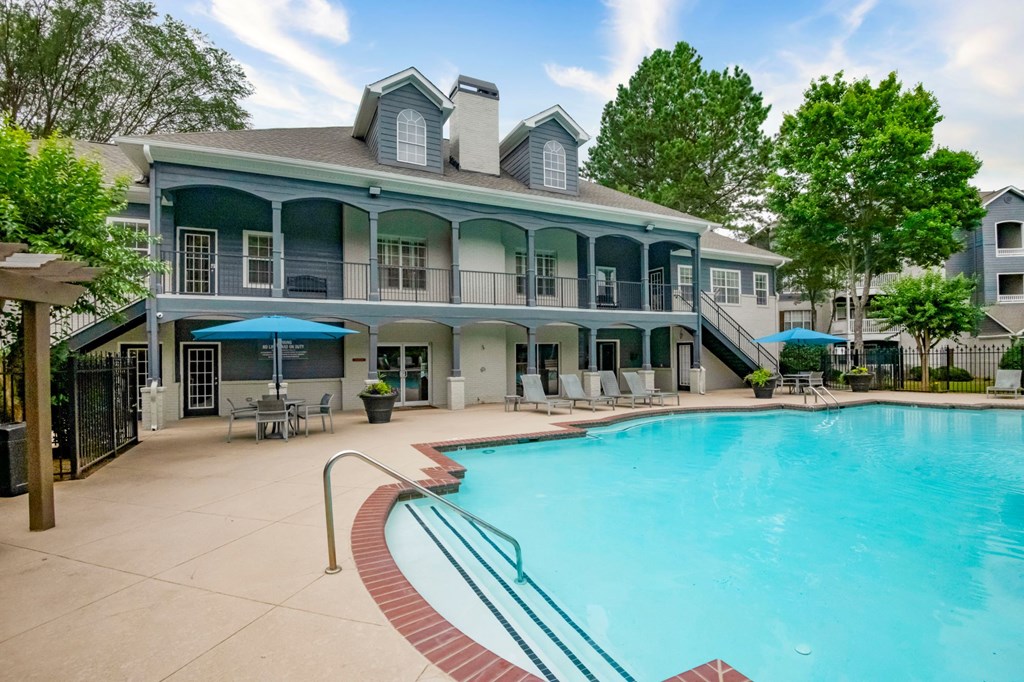 A large swimming pool is surrounded by a patio with chairs and umbrellas.