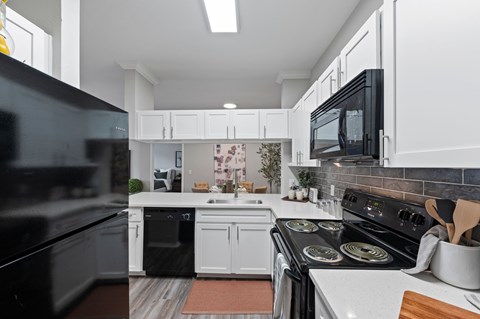 A modern kitchen with black appliances and white cabinets. at The Ambrose, Texas, 77040