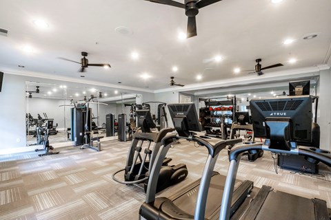 A well-lit gym with treadmills, exercise bikes, and other equipment.