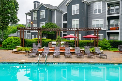 A pool area with chairs and umbrellas in front of a building.