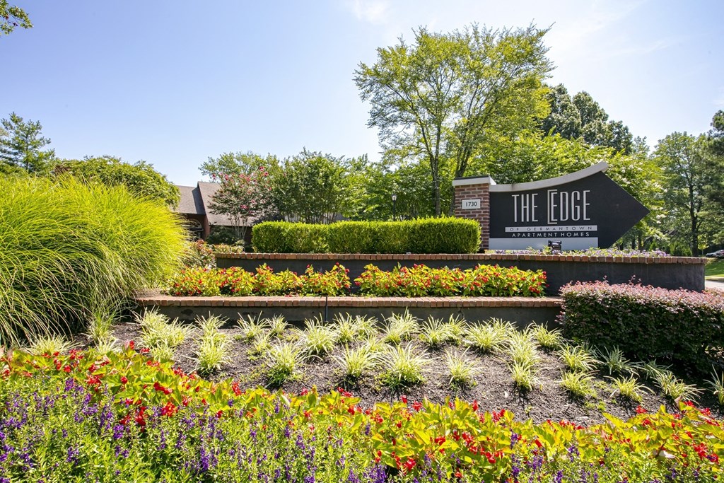 a garden with flowers and bushes in front of a sign that says the edge at The Edge of Germantown, Tennessee