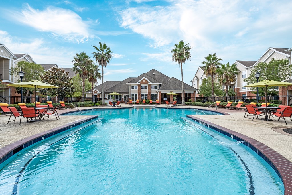 A large swimming pool in a residential area with red lounge chairs and umbrellas. A large swimming pool in a residential area with red lounge chairs and umbrellas at The Fenwick Apartments, Humble, Texas