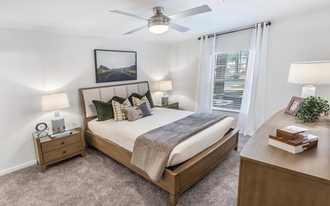 A bedroom with a large bed, a ceiling fan, and a nightstand with a lamp.