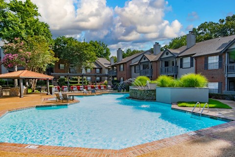 A large swimming pool surrounded by a brick border and a grassy area with a bench.
