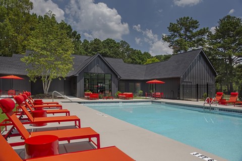 A pool with red chairs and a black building in the background.