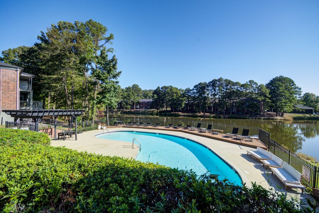 A swimming pool surrounded by greenery and a building in the background.