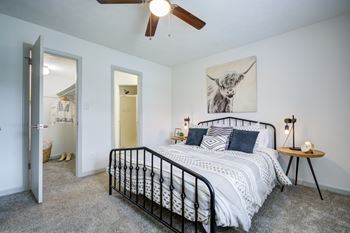 A bedroom with a bed, a ceiling fan, and a painting of a cow on the wall.