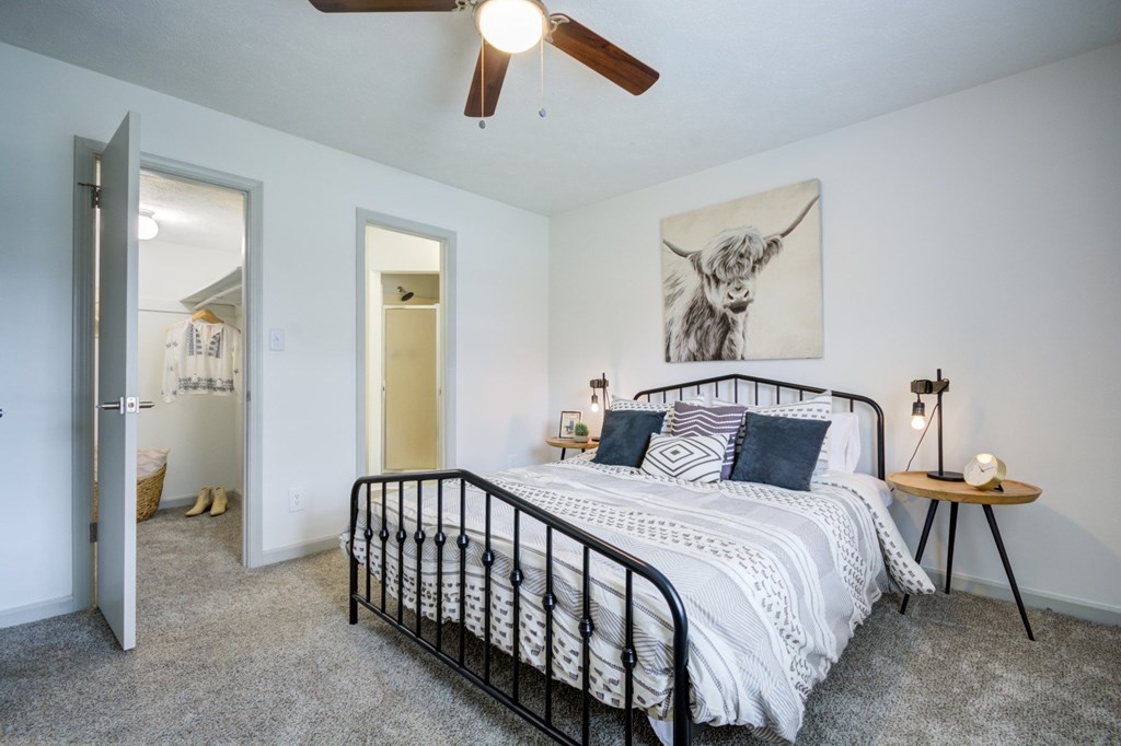 A bedroom with a bed, a ceiling fan, and a painting of a cow on the wall.