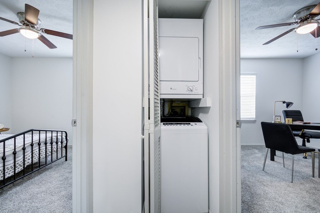 A white refrigerator is in the middle of a room with a ceiling fan.