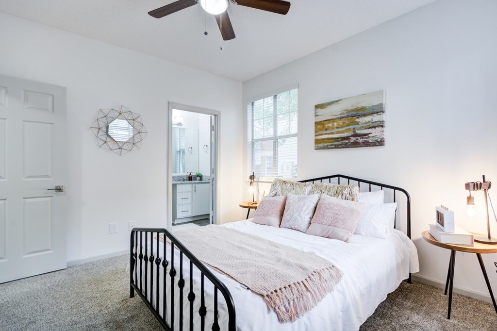 A bedroom with a bed, a ceiling fan, and a painting on the wall.