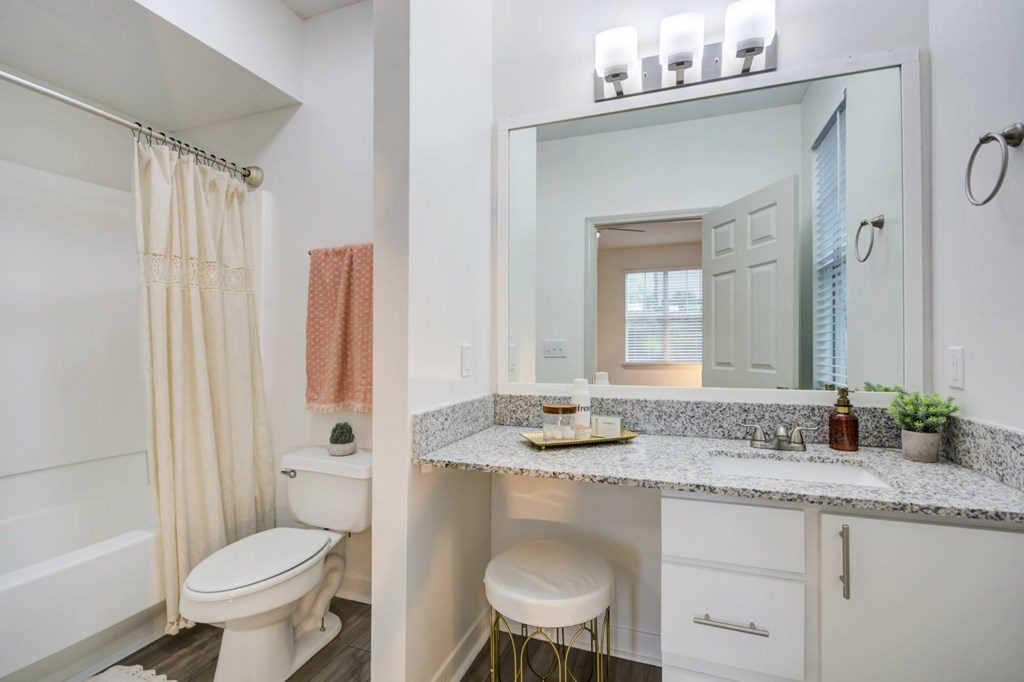 A bathroom with a white toilet, a sink with a marble countertop, and a mirror reflecting a doorway.