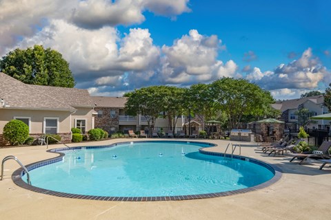 A large outdoor swimming pool surrounded by a concrete patio and a grassy area with trees.