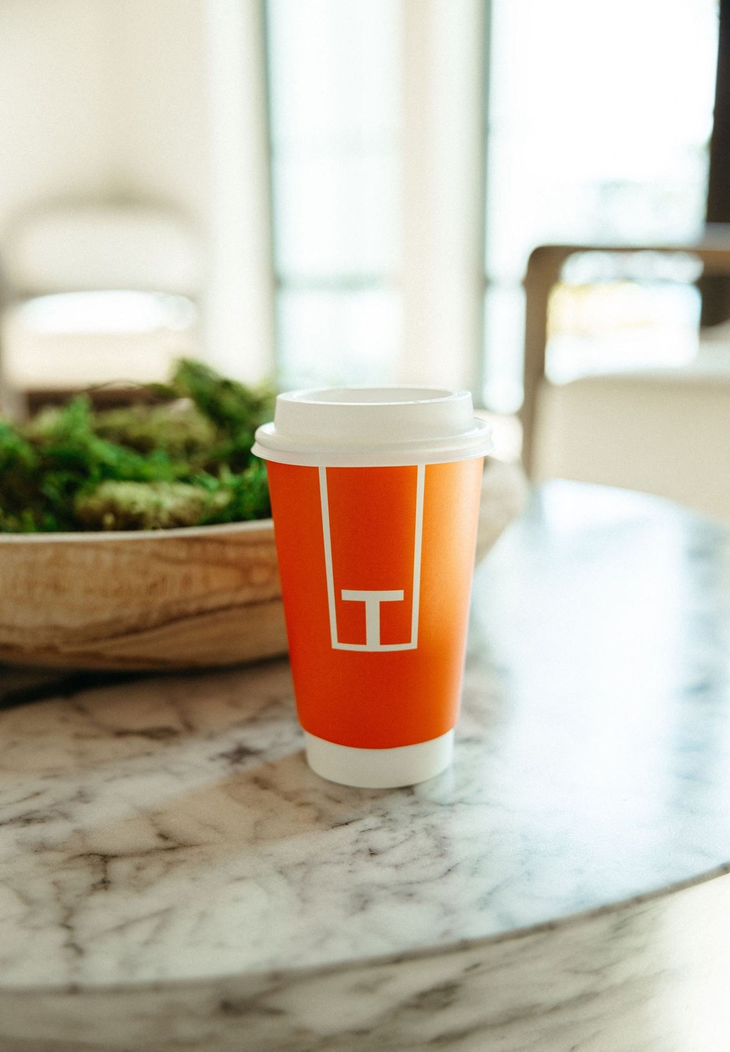 a disposable coffee cup on a table with a bowl of salad