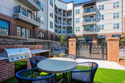 a patio with a table and chairs with an outdoor grill and an apartment building in the background at The Livano Tryon, North Carolina