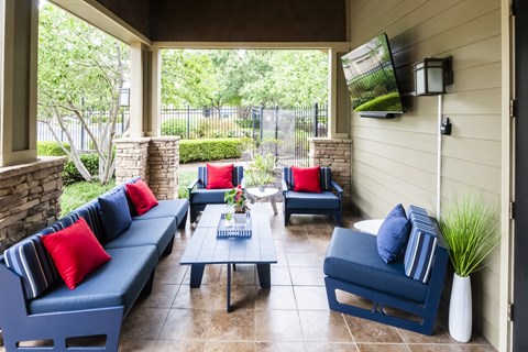 A patio with blue couches and pillows, a coffee table, and a flat screen TV mounted on the wall.