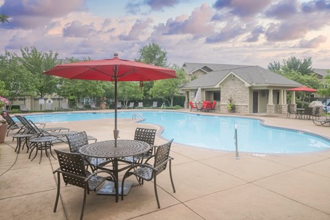 A red umbrella is in front of a pool and a house.