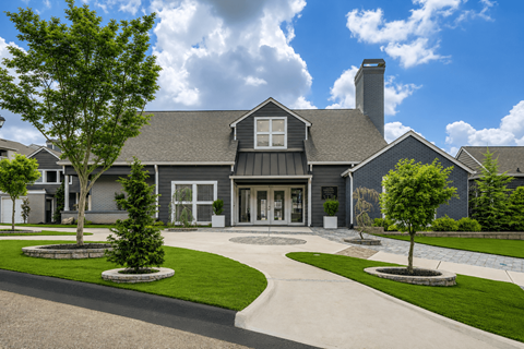 A large house with a grey roof and a chimney is surrounded by a well-manicured lawn and trees.