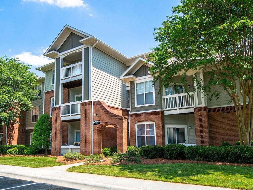 Meticulously maintained grounds with mature trees surround the soft green paint and brick exterior apartment homes at Autumn Park Apartments, Charlotte, NC 28262