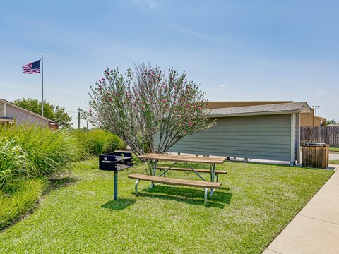 A picnic table is in the grass next to a mailbox and a tree.