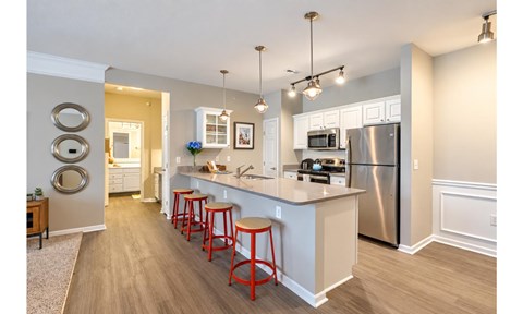 A kitchen with a refrigerator, stove, and bar stools.