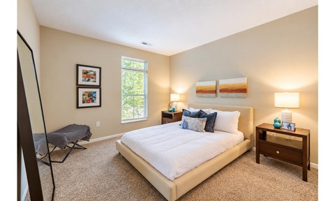 A bedroom with a large bed, a window, and a nightstand with a lamp.