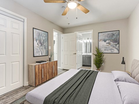 A bedroom with a bed, a ceiling fan, and two framed pictures on the wall.