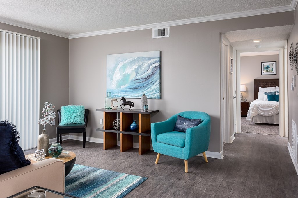 A living room with a blue chair and a painting on the wall.