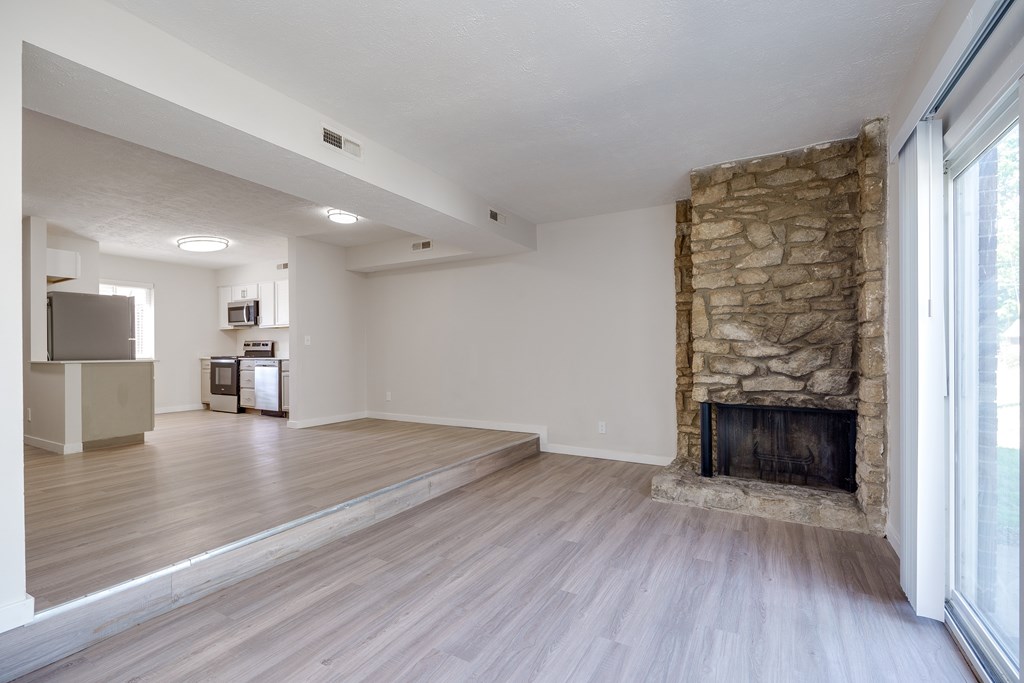 A spacious living room with a stone fireplace and hardwood floors.