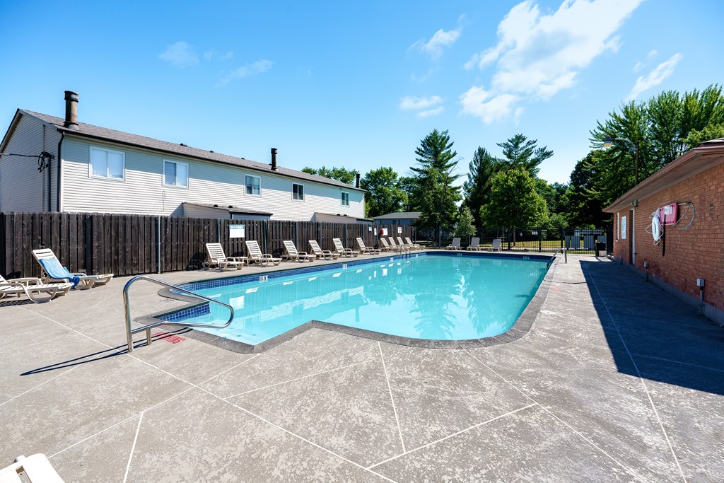 A large outdoor swimming pool surrounded by a concrete patio and a wooden fence.
