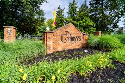 The sign for The Commons is made of brick and is surrounded by plants and flowers.