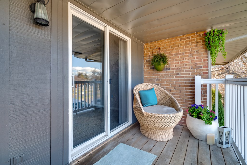 A wicker chair with a blue pillow sits on a wooden deck.